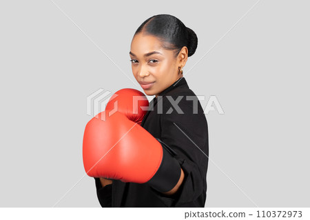 Confident African American businesswoman wearing a black suit with red boxing gloves Confident African American businesswoman wearing a black suit with red boxing gloves 110372973