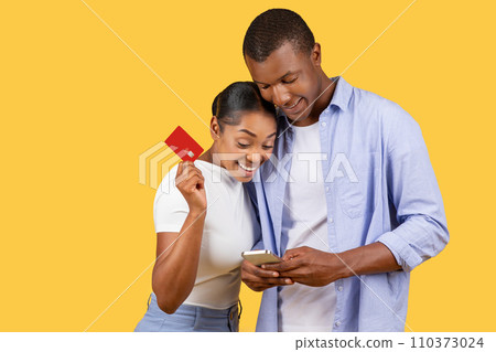 Black couple sharing happy moment with smartphone and credit card on yellow background Black couple sharing happy moment with smartphone and credit card on yellow background 110373024