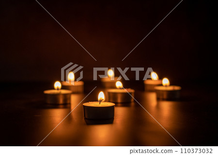 Many candles lit against a black background.Burning candles on dark tableMemory  110373032