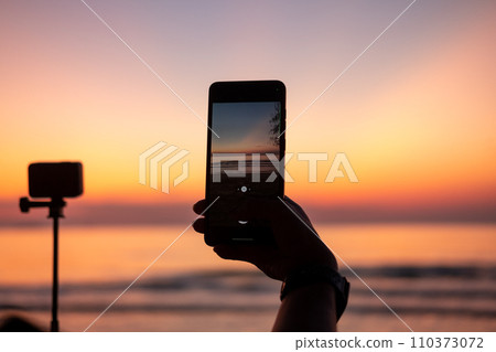 Tourist's hands taking photos of the sea at sunset and twilight. Tourist's hands taking photos of the sea at sunset and twilight. 110373072