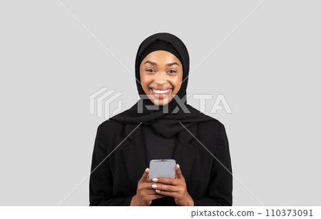 Happy young african american lady in hijab chatting on phone in social networks Happy young african american lady in hijab chatting on phone in social networks 110373091