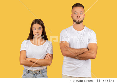Stern-faced young couple with arms crossed in white t-shirts, exuding a strong sense of disagreement 110373123