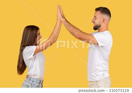 Energetic young couple in white t-shirts happily giving each other a high-five Energetic young couple in white t-shirts happily giving each other a high-five 110373129