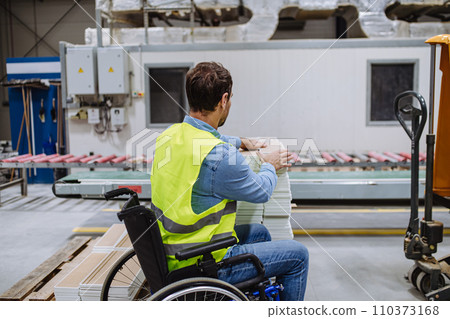 Portrait of man in wheelchair working in modern industrial factory, in adjustable workstation. Concept of workers with disabilities, accessible workplace for employees with mobility impairment. 110373168