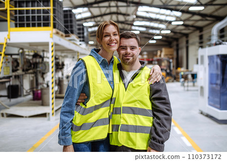 Young man with Down syndrome working in warehouse, colleague talking with him. Concept of workers with disabilities, support in workplace. Young man with Down syndrome working in warehouse, colleague talking with him. Concept of workers with disabilities, support in workplace. 110373172