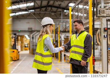 Young man with Down syndrome shaking hands with manager in modern factory. Female manager welcomes new employee in team. Concept of workers with disabilities, support in workplace. Young man with Down syndrome shaking hands with manager in modern factory. Female manager welcomes new employee in team. Concept of workers with disabilities, support in workplace. 110373247