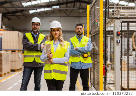 Portrait of team of warehouse employees standing in warehouse. Team of workers and female manger in modern industrial factory, heavy industry, manufactrury. Concept of team management. Portrait of team of warehouse employees standing in warehouse. Team of workers and female manger in modern industrial factory, heavy industry, manufactrury. Concept of team management. 110373253