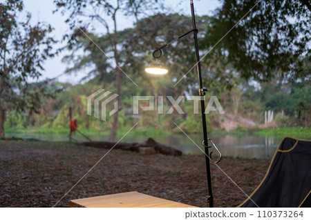 A light shines on a wooden camping table near a stream. 110373264