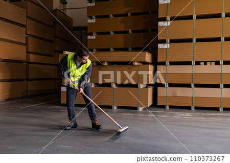 Portrait of young man with Down syndrome sweeping the floor, working in factory, warehouse. Concept of workers with disabilities, support in workplace. Portrait of young man with Down syndrome sweeping the floor, working in factory, warehouse. Concept of workers with disabilities, support in workplace. 110373267