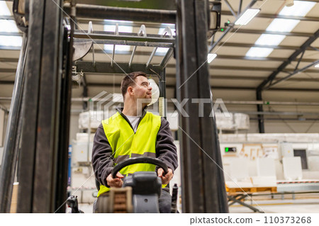 Portrait of young man with Down syndrome driving forklift, working in factory, warehouse. Concept of workers with disabilities, support in workplace. 110373268