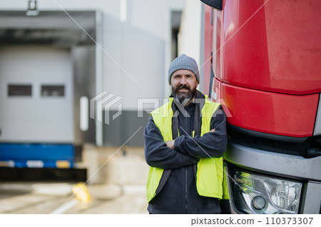Truck driver standing with arms crossed leaning on red truck and looking at camera. 110373307