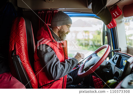 Truck driver sitting in truck, holding tablet, looking at cargo details, delivery schedule. 110373308