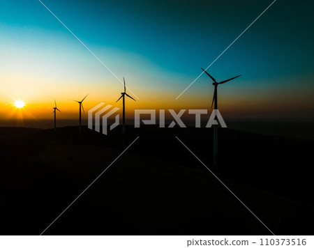 Aerial landscape photography of sunrise over nature with wind turbines. Windmill in soft morning light with forest, trees around. Concept of wind power as clean, renewable energy source. 110373516