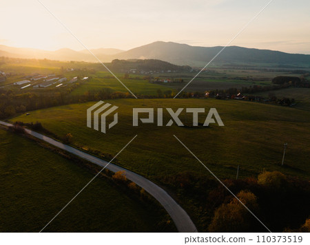 Aerial view of green summer farm fields, crops or pasture with road during sunset. Aerial view of green summer farm fields, crops or pasture with road during sunset. 110373519