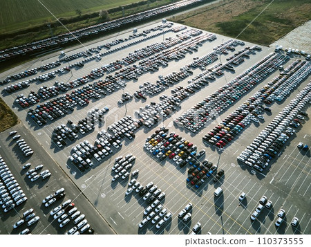 Aerial view of a massive parking lot at a car manufacturing facility with newly produced vehicles parked in rows. 110373555