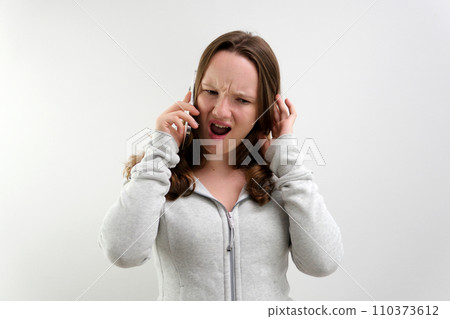 Frustrated annoyed sad woman with mobile phone standing intside white background 110373612