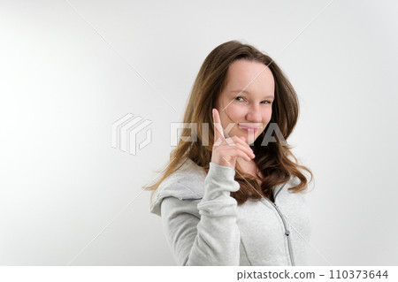 a young teenage girl raised her index finger up, squinting her eyes, there is an idea, a trick, happy, on a white background, space for advertising text a young teenage girl raised her index finger up, squinting her eyes, there is an idea, a trick, happy, on a white background, space for advertising text 110373644