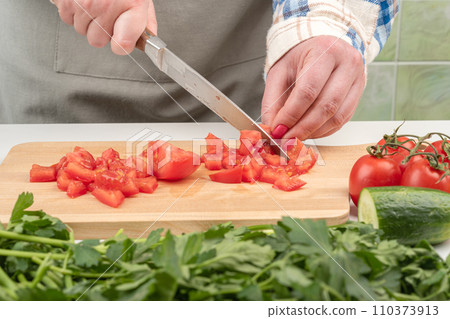 A juicy tomato is cut into small pieces on a wooden cutting board. A juicy tomato is cut into small pieces on a wooden cutting board. 110373913