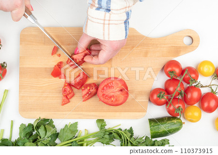 Female hands cut a tomato into small pieces on a cutting board. 110373915