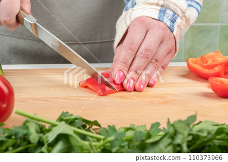 Female hands with manicure cut a piece of sweet pepper on a wooden cutting board. Female hands with manicure cut a piece of sweet pepper on a wooden cutting board. 110373966