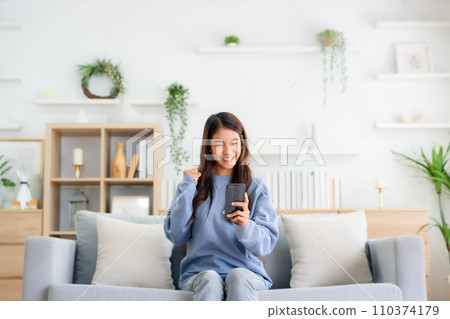 Happy young asian woman relax on comfortable couch at home texting messaging on smartphone 110374179