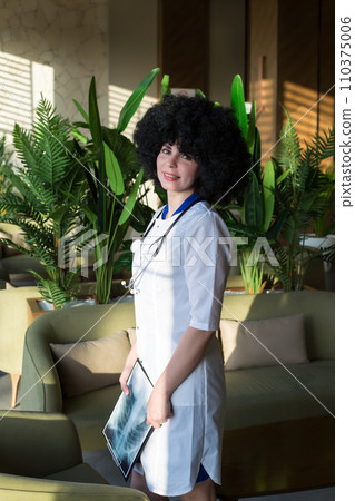 Young beautiful girl nurse with black curly hair in a lab coat Young beautiful girl nurse with black curly hair in a lab coat 110375006