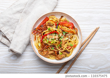 White bowl with Chow Mein or Lo Mein, traditional Chinese stir fry noodles with meat and vegetables, served with chopsticks top view on rustic white wooden background table 110375475