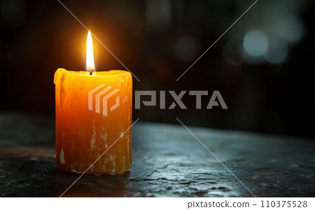 A single candle burning brightly in a dark room, casting a gentle glow. The candle symbolizes remembrance and awareness 110375528