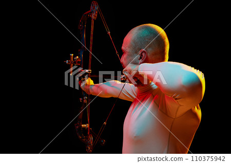 Back view image of man, archery at hele aiming with archery bow on target against black studio background in neon light. Archery sport, competition 110375942