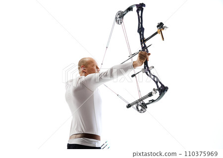 Bald man in his 40s, archery athlete exercising with the bow, aiming upwards isolated over white studio background. Archery sport, competition 110375969