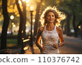 Mature blond woman jogging in the park at sunset 110376742
