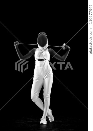 Portrait of swordswoman posing with her dual blades resting on her shoulders against black studio background in monochrome filter. Portrait of swordswoman posing with her dual blades resting on her shoulders against black studio background in monochrome filter. 110377945