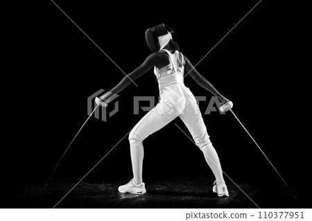 Dual-blade mastery portrait of female fencing maestro, confidently posing with two swords against black studio background. Artistry and precision of sport 110377951