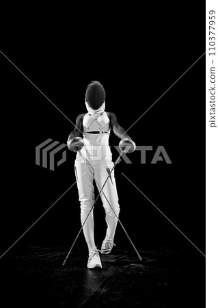 Skilled female posing, gracefully crossing swords in intricate dance of precision and poise against black studio background. 110377959