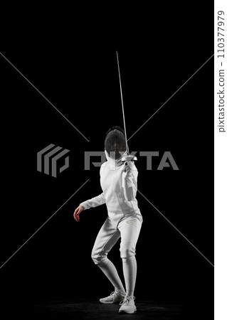 Swordswoman, professional female fencer's poised stance, against black studio background. Intensity and excitement of fencing. Swordswoman, professional female fencer's poised stance, against black studio background. Intensity and excitement of fencing. 110377979