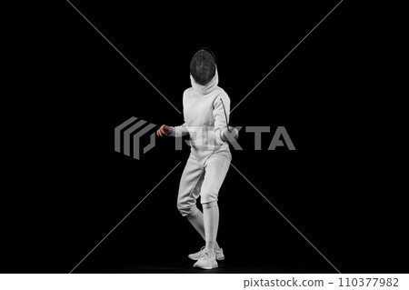 Energy portrait of female fencer lunges forward, her blade poised to strike against black studio background. Copy space 110377982