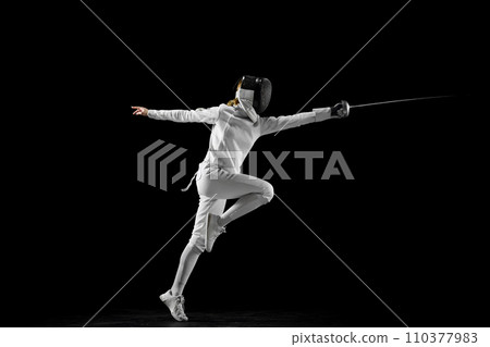 Confidence and strength. Female athlete in fencing gear showcasing her impeccable form, sword poised for action against a black studio background. Confidence and strength. Female athlete in fencing gear showcasing her impeccable form, sword poised for action against a black studio background. 110377983