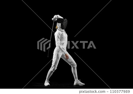 Fencer's flawless attack, precision evident in her form against black studio background, epitomizing pursuit of perfection. Concept of active lifestyle. 110377989