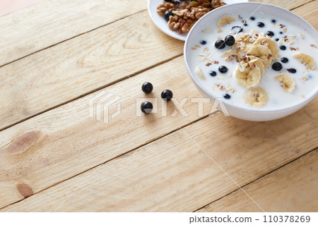 Oatmeal porridgewith bananas, nuts, raisins, blueberries and milk on table on wooden  background.  Healthy breakfast and diet food. Top view 110378269