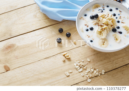 Oatmeal porridgewith bananas, nuts, raisins, blueberries and milk on table on wooden  background.  Healthy breakfast and diet food. Top view 110378277