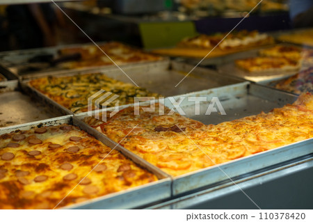 Authentic Italian pizza in a restaurant display window. Various pizzeria in glass window display. Focus on pizza with tomatoes 110378420