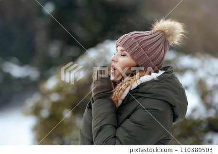 woman outdoors in park in winter warming cold hands with breath 110380503