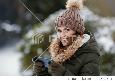 happy woman outdoors in park in winter using phone 110380504