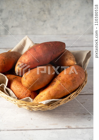 Whole raw sweet potatoes in a basket, on bright background, top view. Whole raw sweet potatoes in a basket, on bright background, top view. 110380518