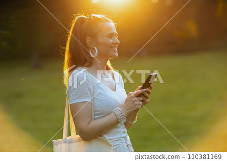 happy trendy woman using smartphone in meadow outdoors 110381169