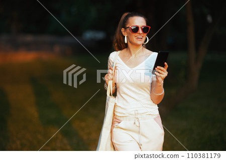 smiling stylish woman in shirt using phone and walking smiling stylish woman in shirt using phone and walking 110381179