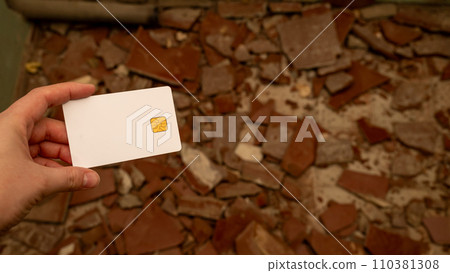 Woman's hand with a bank card against the background of pieces of broken tiles on the floor. The concept of starting repairs and the high cost of repairs. 110381308