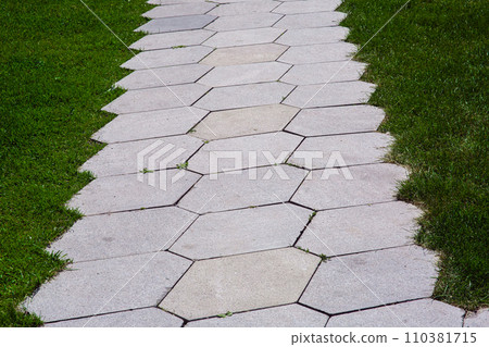 pavement with stone tiles honeycomb pattern on park with green lawn lit by sunlight close-up, nobody. pavement with stone tiles honeycomb pattern on park with green lawn lit by sunlight close-up, nobody. 110381715