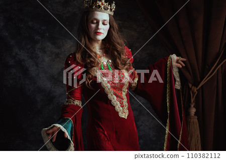 medieval queen in red dress with white makeup and crown 110382112