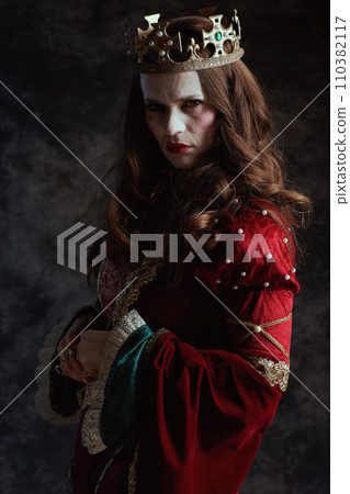 scary medieval queen in red dress with white makeup and crown 110382117